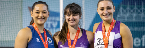 Three athletes stand on a podium. The University of Portsmouth athlete has a gold medal